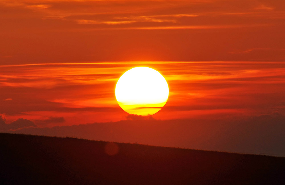 The sun is setting over a hill.